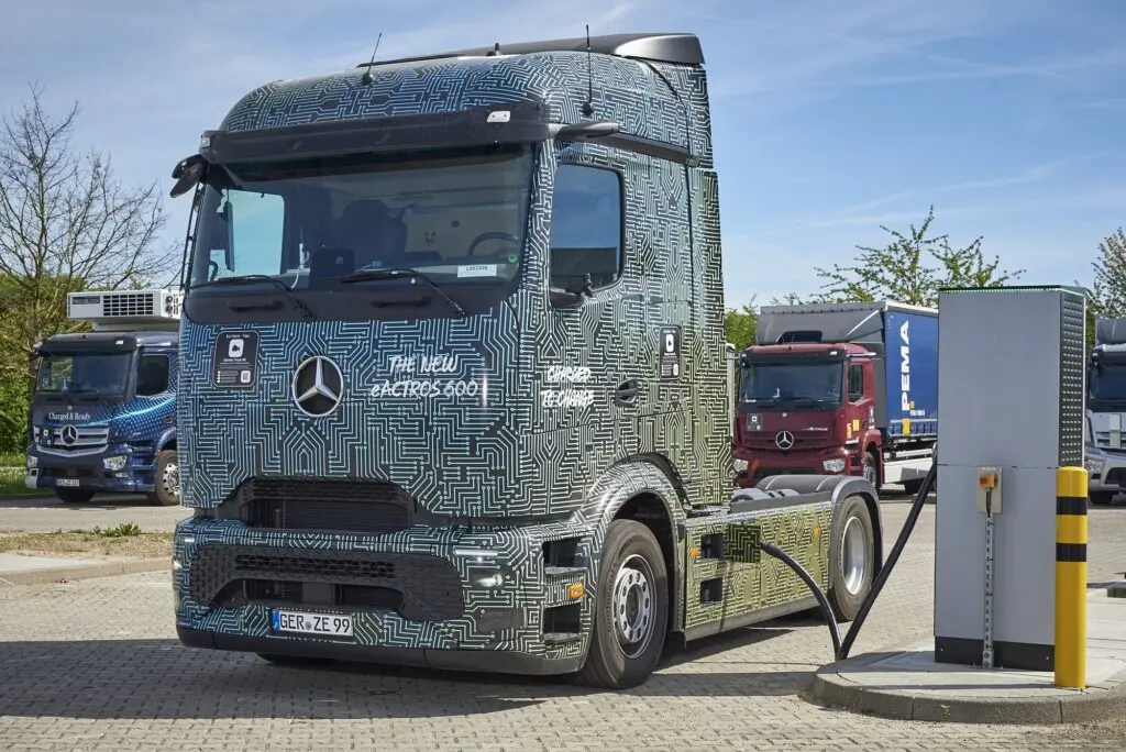 A camouflaged Mercedes-Benz eActros 600 truck connected to a charging station during testing.