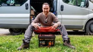 A person seated beside a Lithink battery in front of a camper van; image from the Lithink Care+ website.