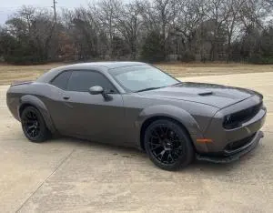 Gray Dodge Challenger with widebody panels and black wheels, photographed from the front left.